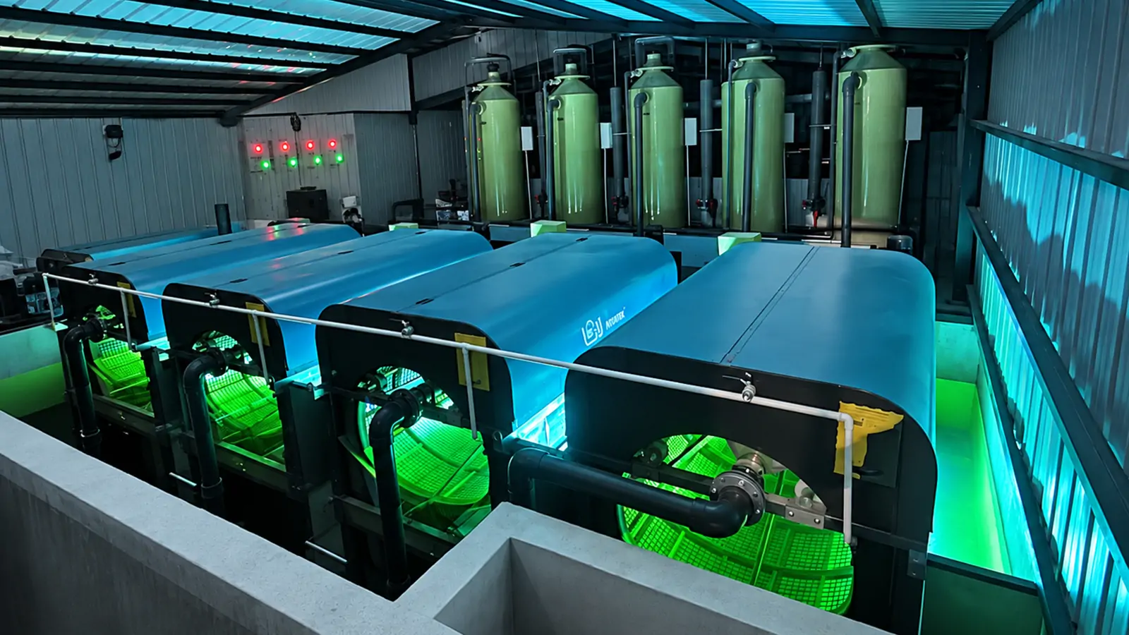 Blue drum filters beside vertical water-treatment vessels inside a RAS equipment building
