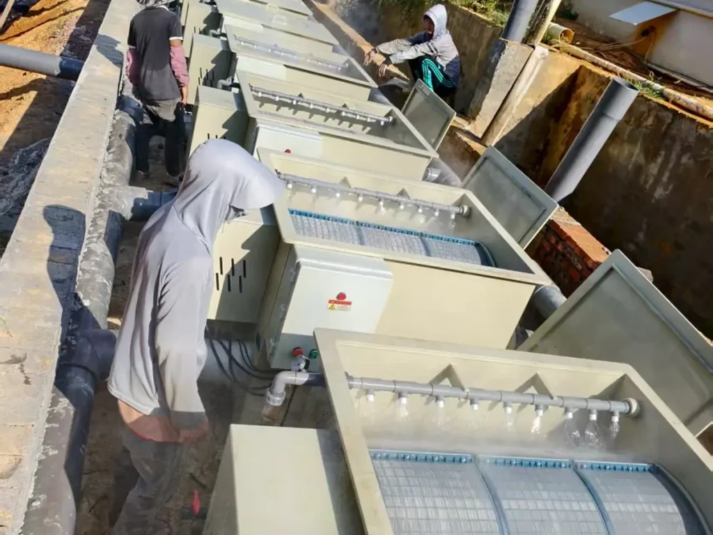 Workers beside a row of open filter units and spray pipes.