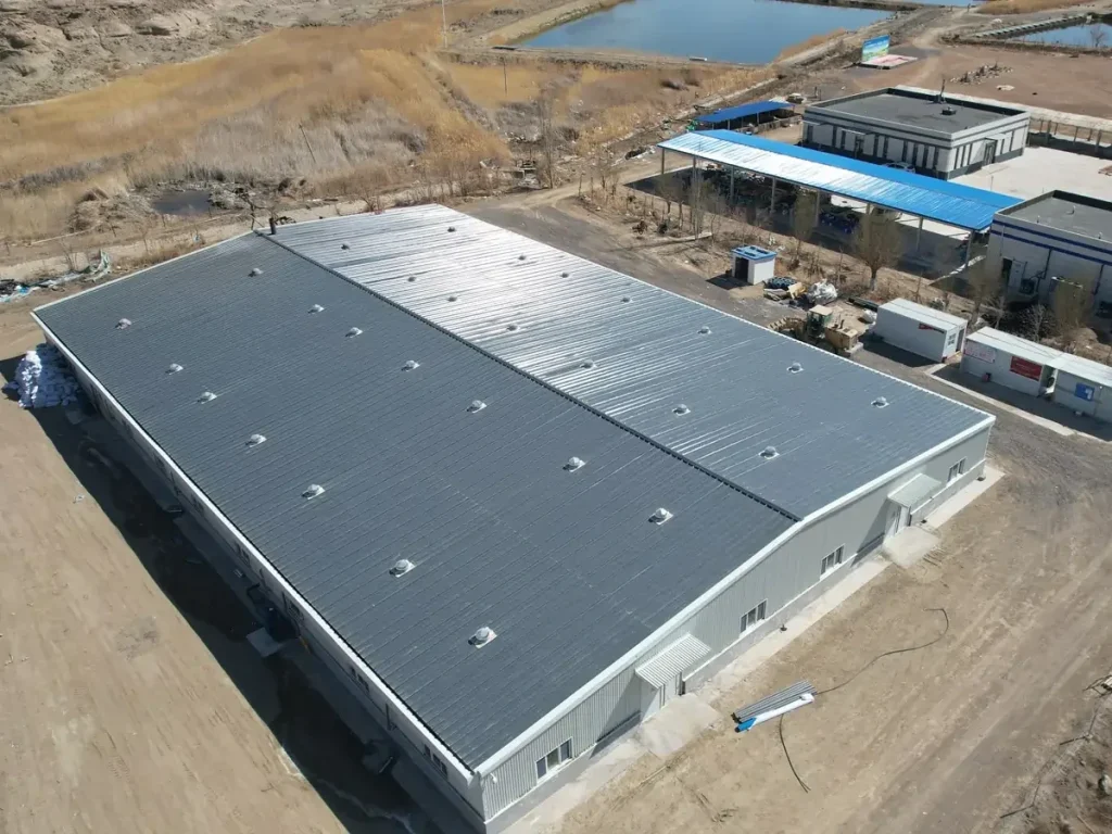 Oblique aerial view of a large gray-roofed building beside outdoor water bodies.