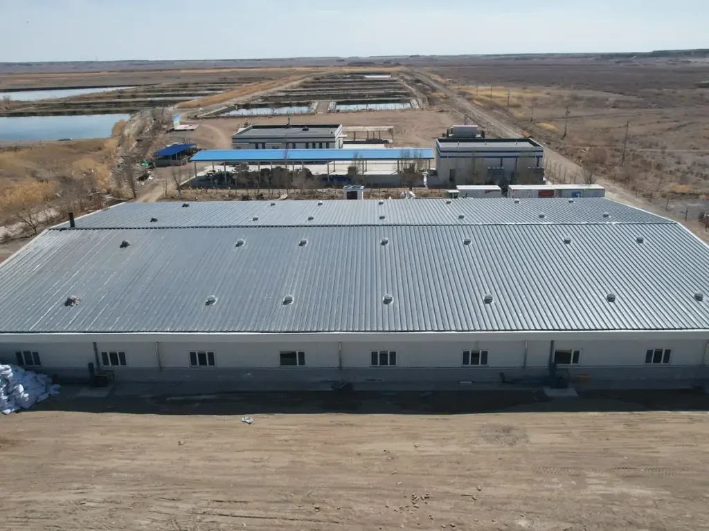 Gray-roofed aquaculture building with adjacent buildings, access roads and outdoor ponds.
