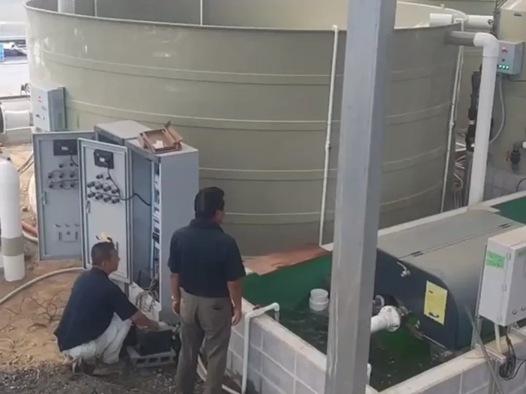 Workers beside an open control cabinet and installed pipework.
