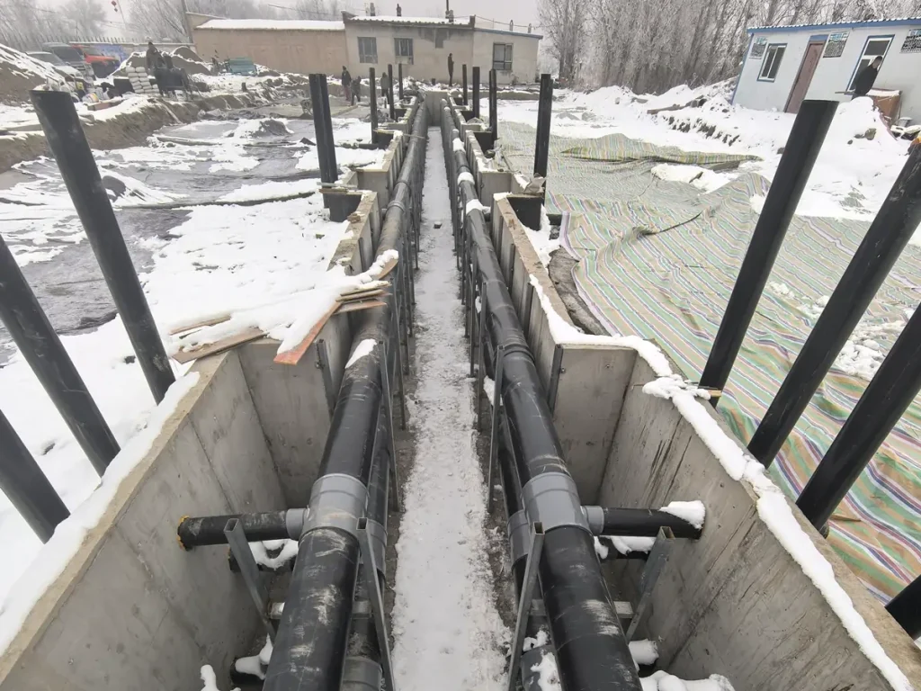 Large pipes in an open trench beside a paved area with snow.
