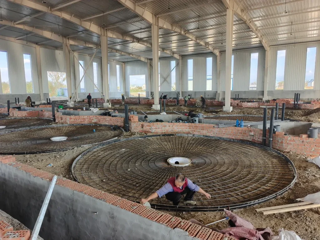 Circular reinforcement cages and workers preparing tank bases inside the building.