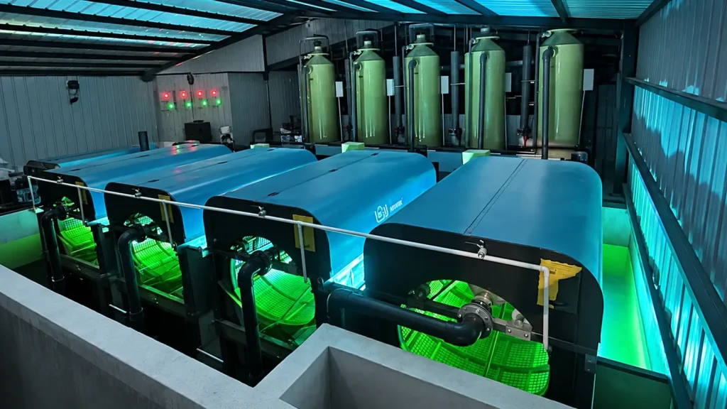 Blue-covered filtration units, vertical vessels and connecting pipes inside a roofed enclosure.