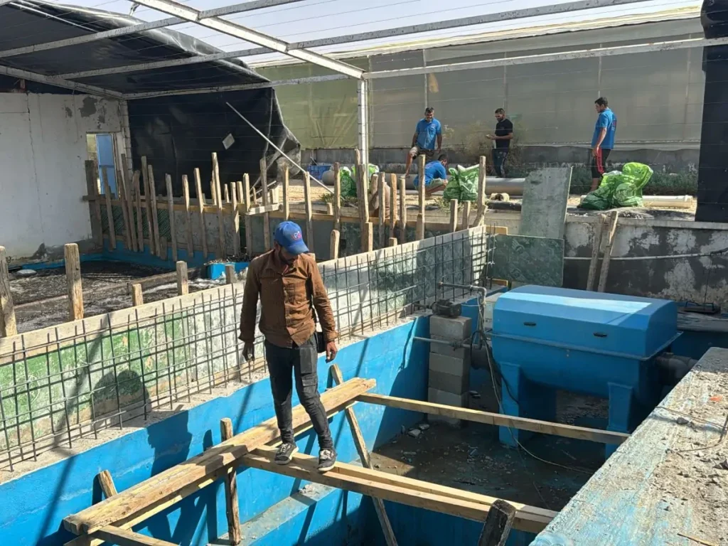 Workers beside reinforcement bars, concrete compartments and a blue filter unit.
