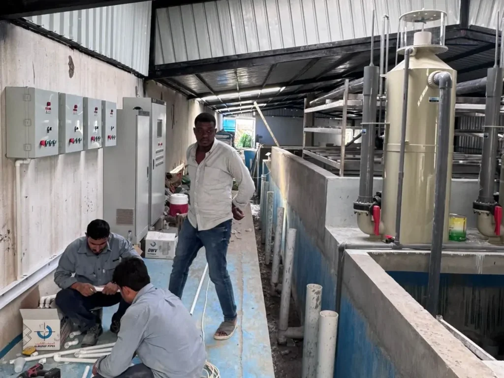 People beside vertical treatment vessels, control panels and concrete compartments.