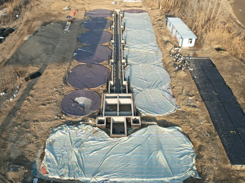 Aerial construction-stage view of covered tank foundations and a central service corridor at Wujiaqu.