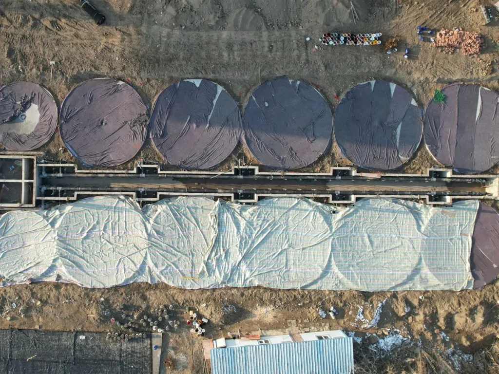 Overhead view of pipework between covered tank foundations during construction of the Wujiaqu shrimp facility.