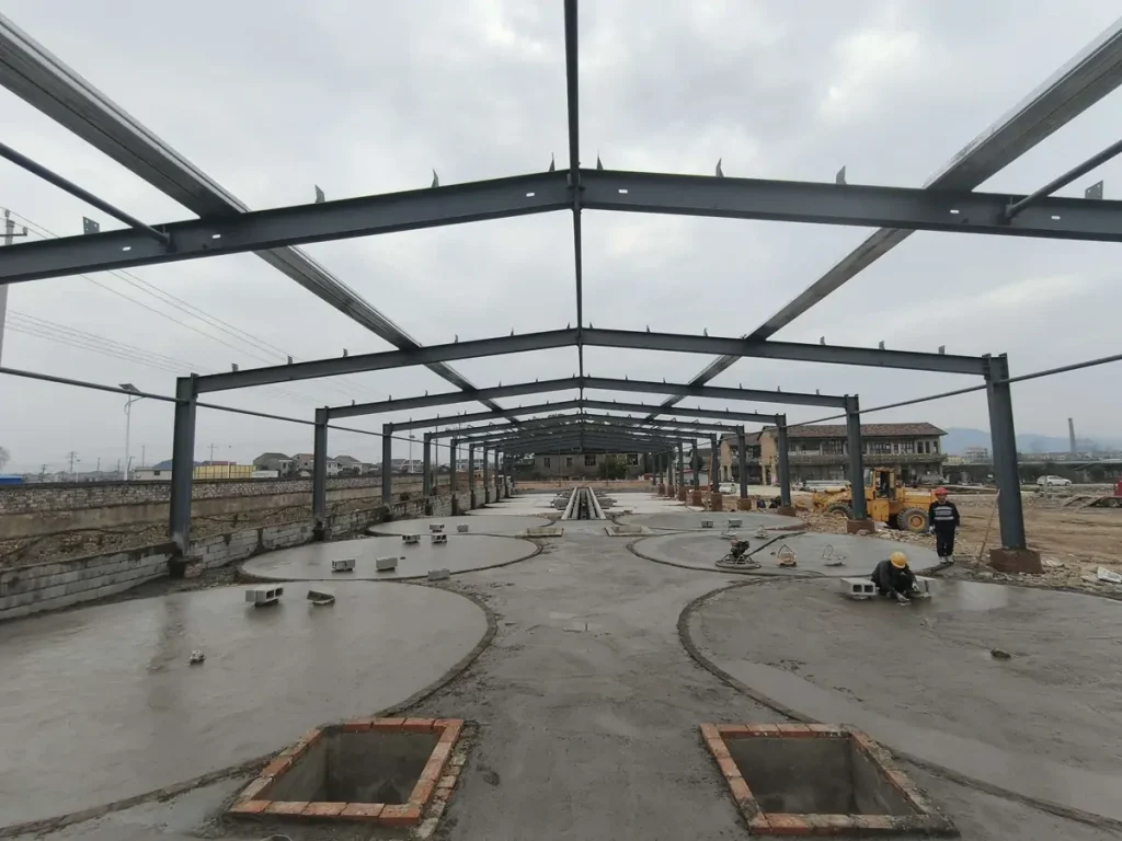 Circular concrete pads and workers beneath an open steel building frame.