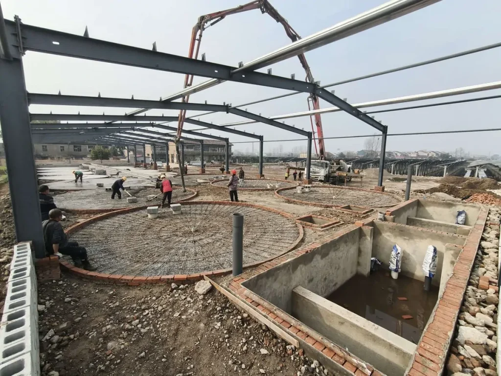 Workers and a concrete-pump boom beside reinforced tank foundations.