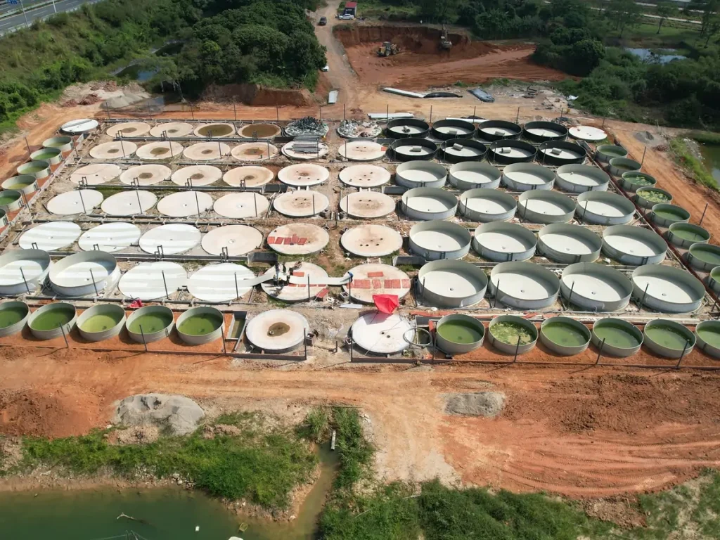 Rows of circular tanks and unfinished tank bases with connecting pipes across the outdoor site.